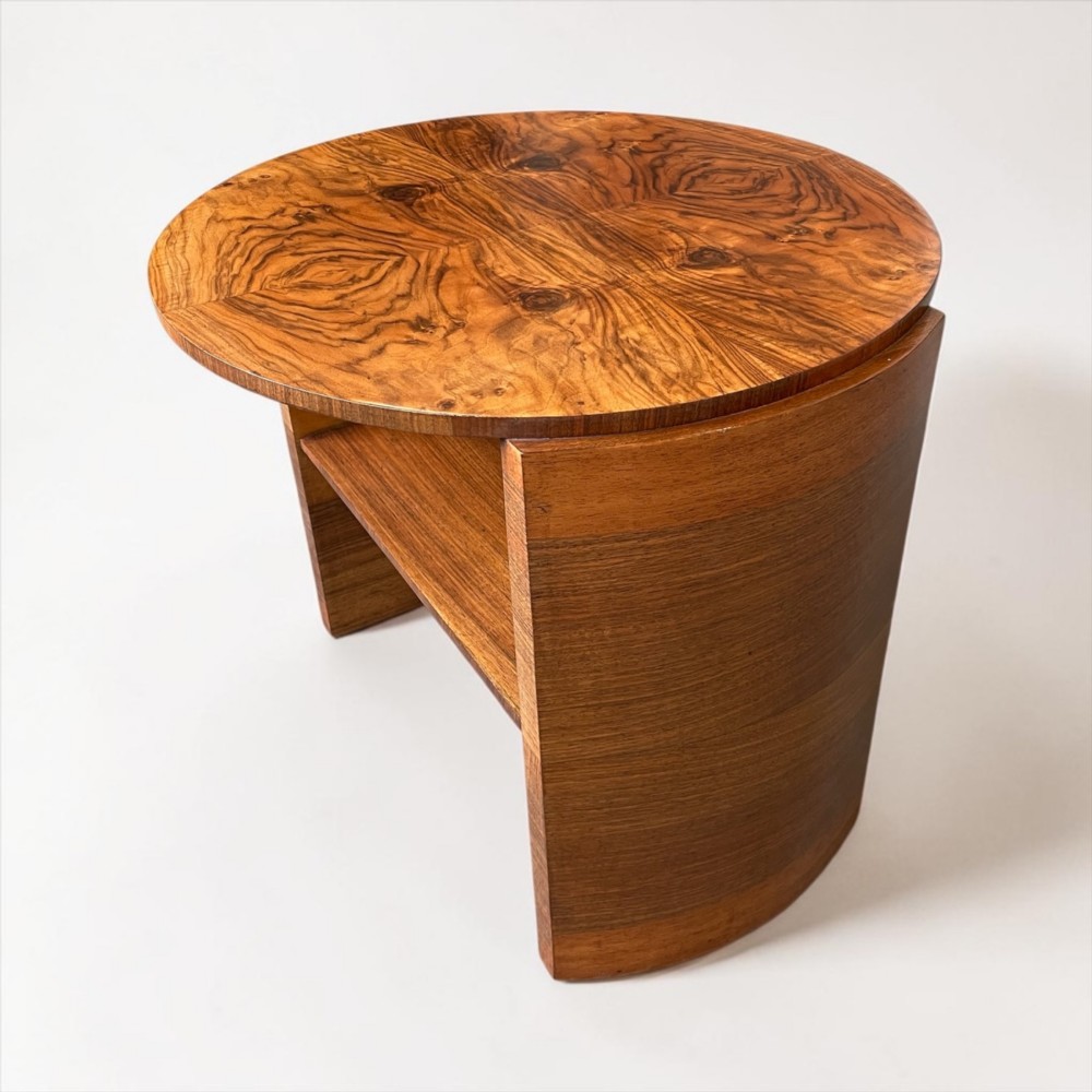 A circular Art Deco coffee table made of figured walnut veneer with a quartered top pattern, curved side supports, and an lower shelf. View III