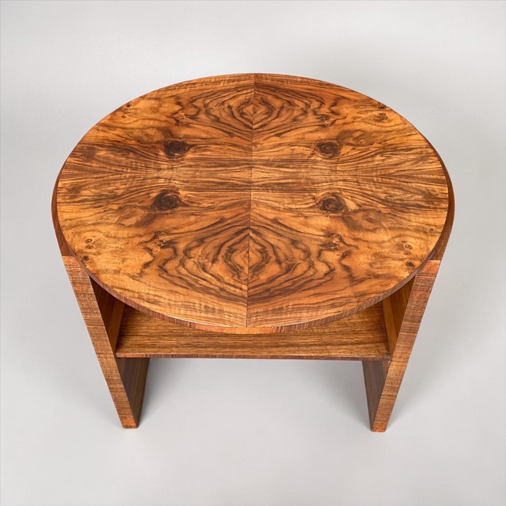 A circular Art Deco coffee table made of figured walnut veneer with a quartered top pattern, curved side supports, and an lower shelf. View V