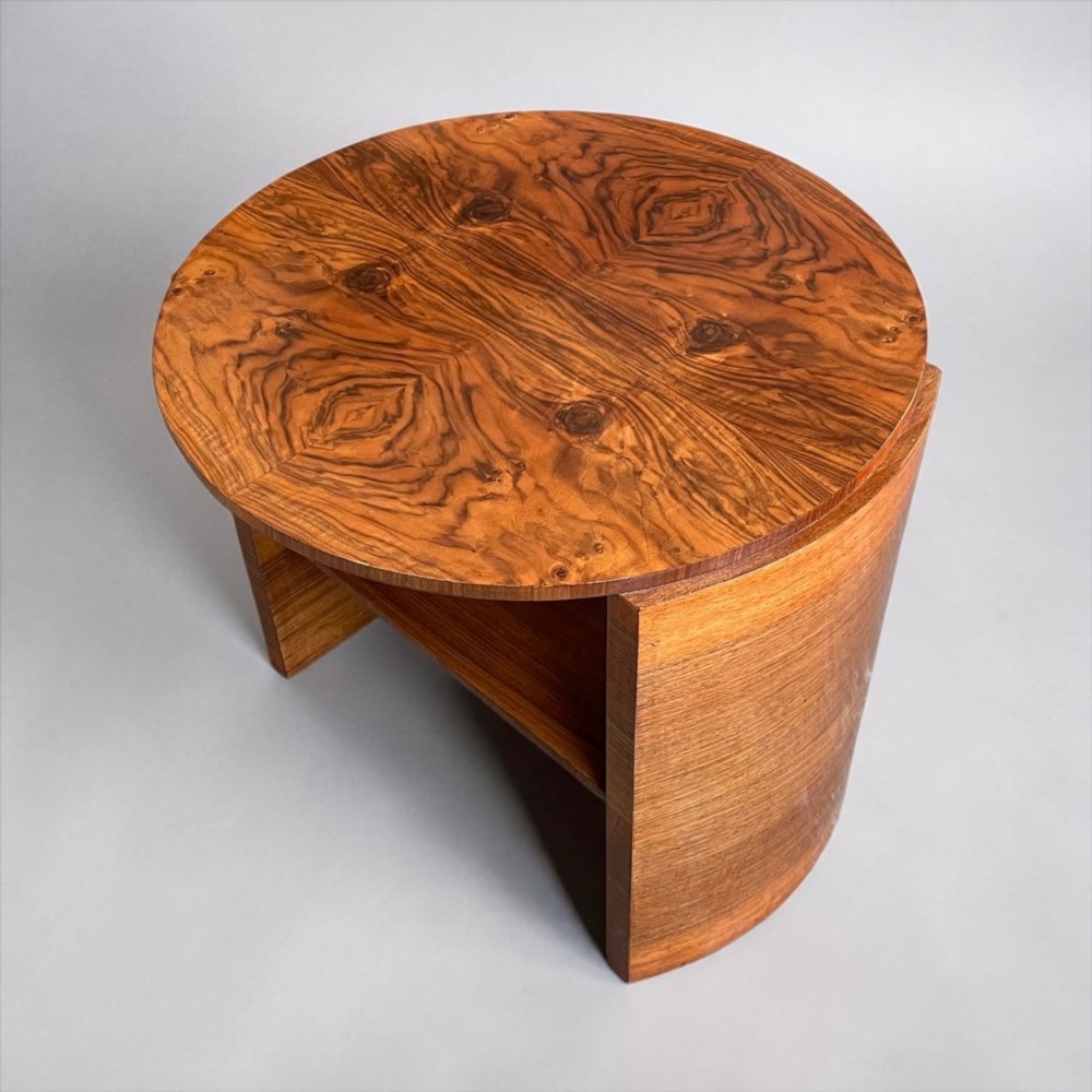 A circular Art Deco coffee table made of figured walnut veneer with a quartered top pattern, curved side supports, and an lower shelf. View VII