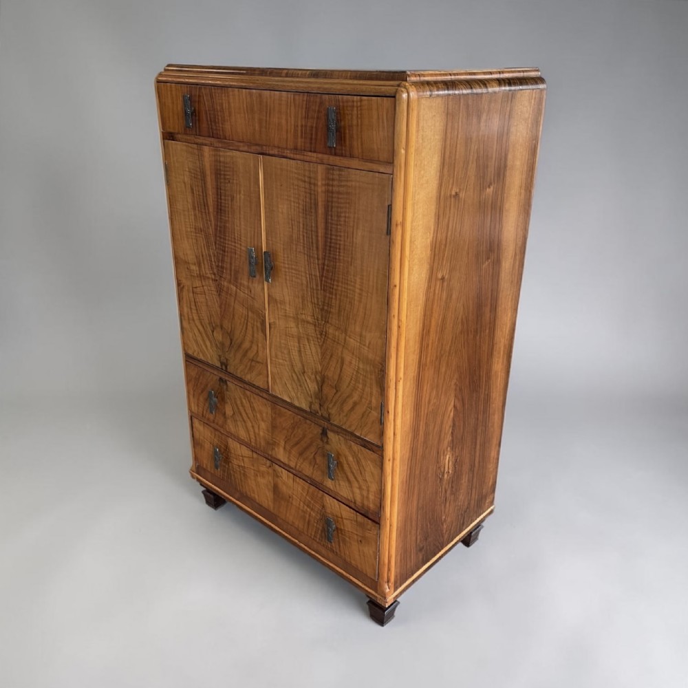 An Art Deco figure-grained walnut tallboy cabinet with rounded top corners, a top drawer, central double doors, and two lower drawers with metal handles.