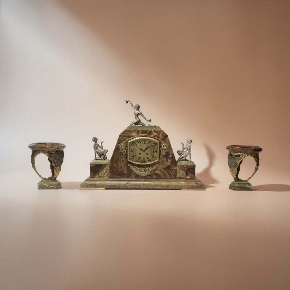 An Art Deco French mantel clock crafted from stepped brown and green onyx with silvered figural sculptures, accompanied by two matching side garnitures.