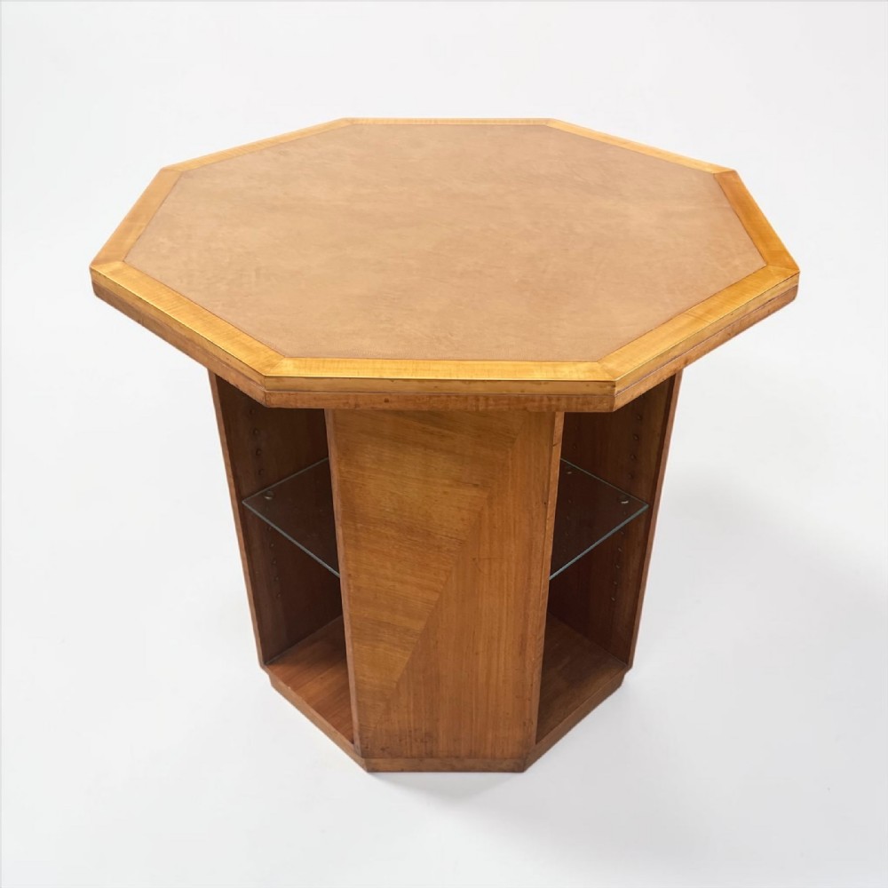 An octagonal Art Deco occasional table in light brown wood veneer featuring open side alcoves with glass shelves.