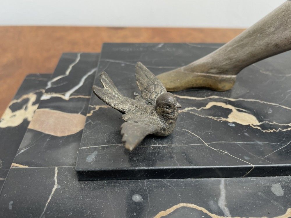 An Art Deco bronze sculpture depicting a seated woman holding a thin rod surrounded by small birds on a tiered black and gold marble base. View IX