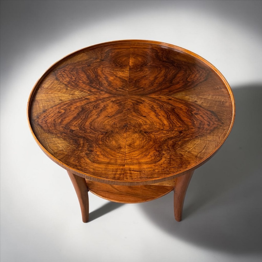 A circular Art Deco walnut side table featuring a quarter-matched book-veneered top, a lower circular shelf, and curved legs.