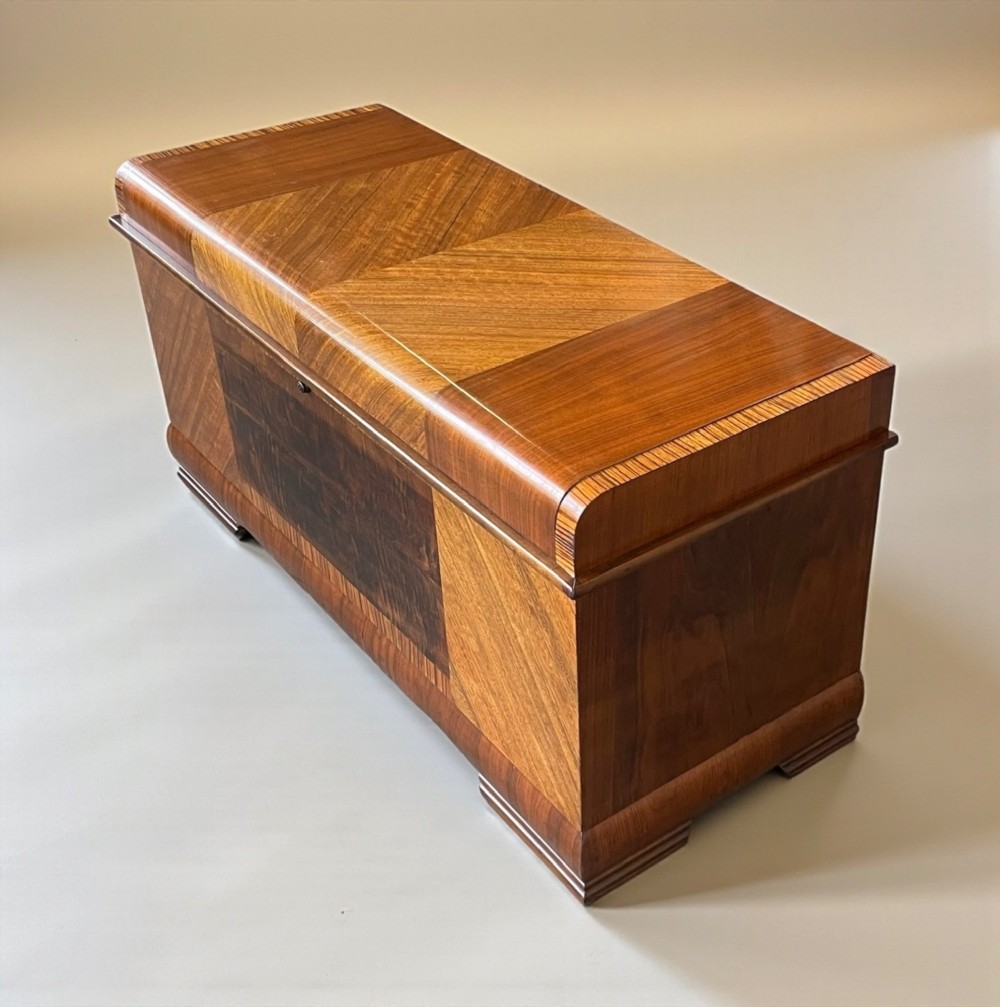 An Art Deco timber blanket chest featuring geometric chevron wood veneers and rounded waterfall edges on a stepped plinth base.