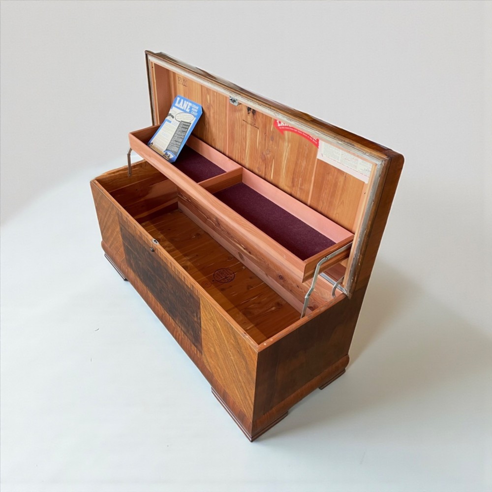 An Art Deco timber blanket chest featuring geometric chevron wood veneers and rounded waterfall edges on a stepped plinth base. View II