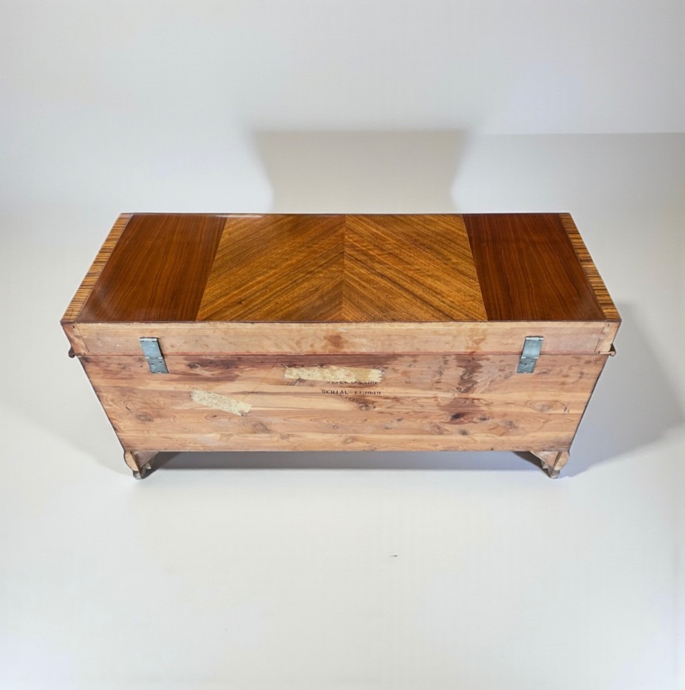 An Art Deco timber blanket chest featuring geometric chevron wood veneers and rounded waterfall edges on a stepped plinth base. View IX