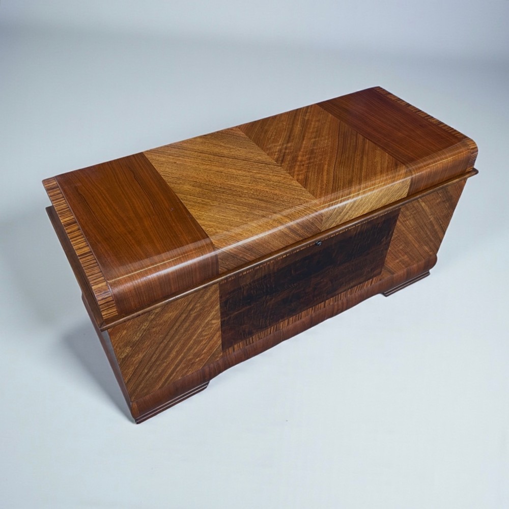 An Art Deco timber blanket chest featuring geometric chevron wood veneers and rounded waterfall edges on a stepped plinth base. View XI