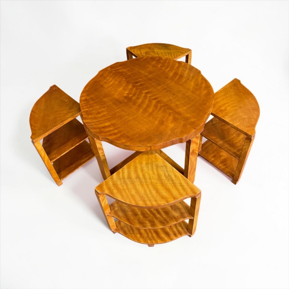 An Art Deco golden timber nest of five tables consisting of a central circular table encircled by four matching tiered wedge tables.