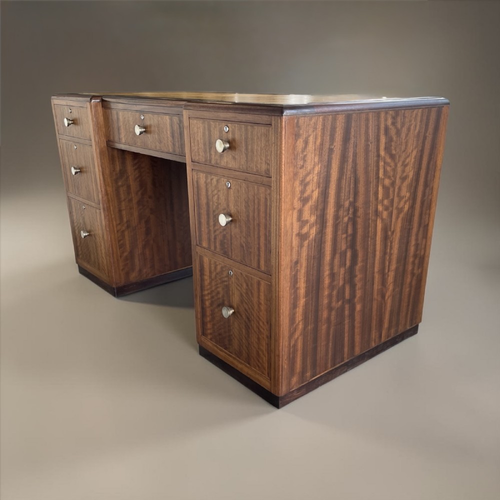 An Art Deco twin-pedestal executive desk featuring figured wood grain veneer, round metal knobs, and a central kneehole with drawers.