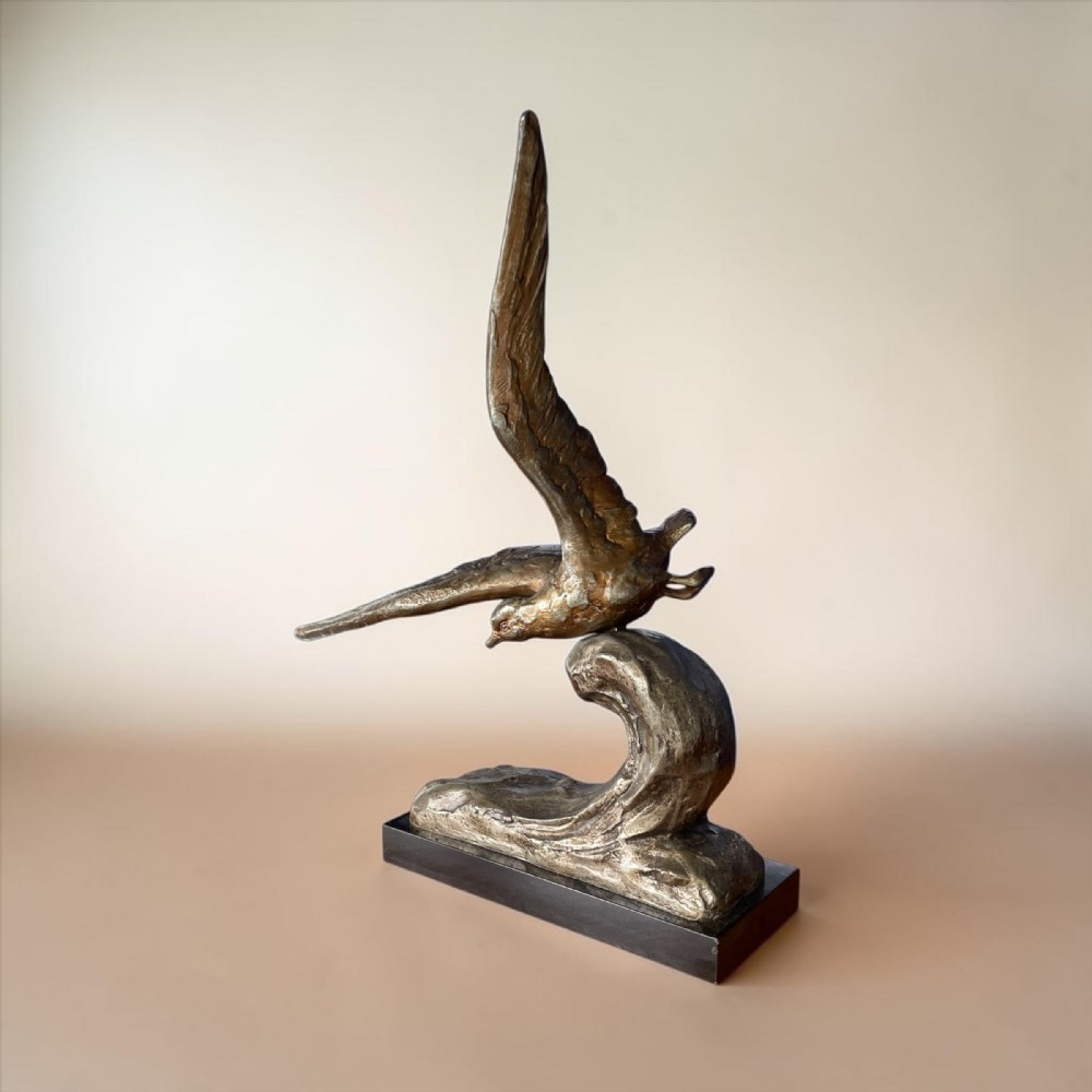 An Art Deco patinated bronze sculpture depicting an albatross with extended wings rising above a carved wave formation, mounted on a rectangular dark marble base.