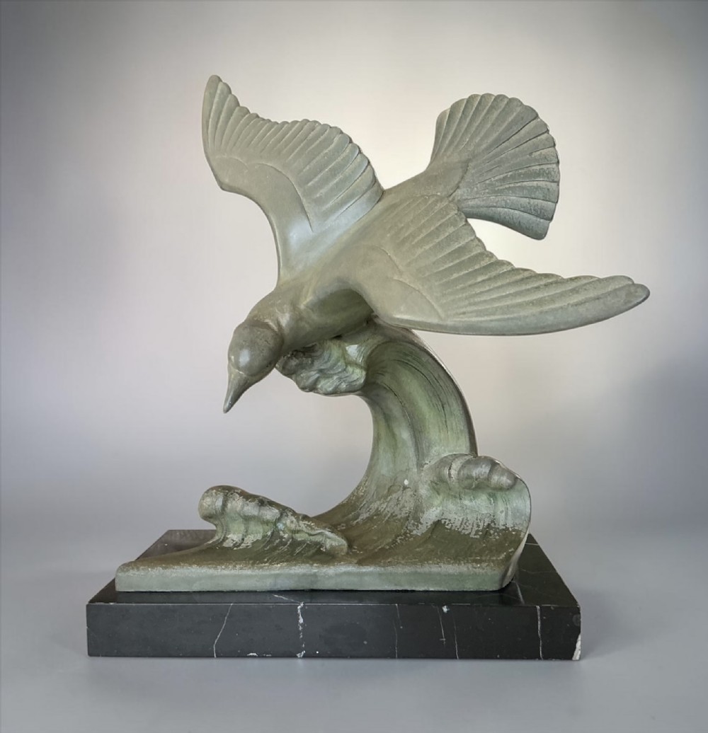 An Art Deco verdigris green patinated metal sculpture depicting a seagull swooping over stylised ocean waves, mounted on a dark marble base.