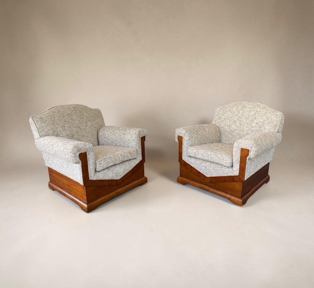 A pair of Art Deco lounge chairs featuring light beige textured upholstery and angular walnut bases.