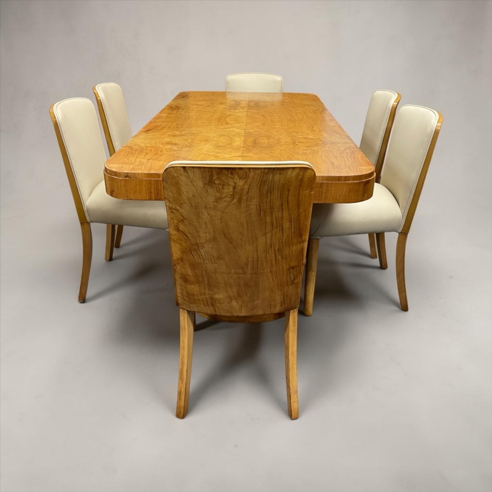 An Art Deco burr walnut dining table featuring rounded corners and a central pedestal base, accompanied by six matching cloud-back chairs upholstered in off-white leather. View III