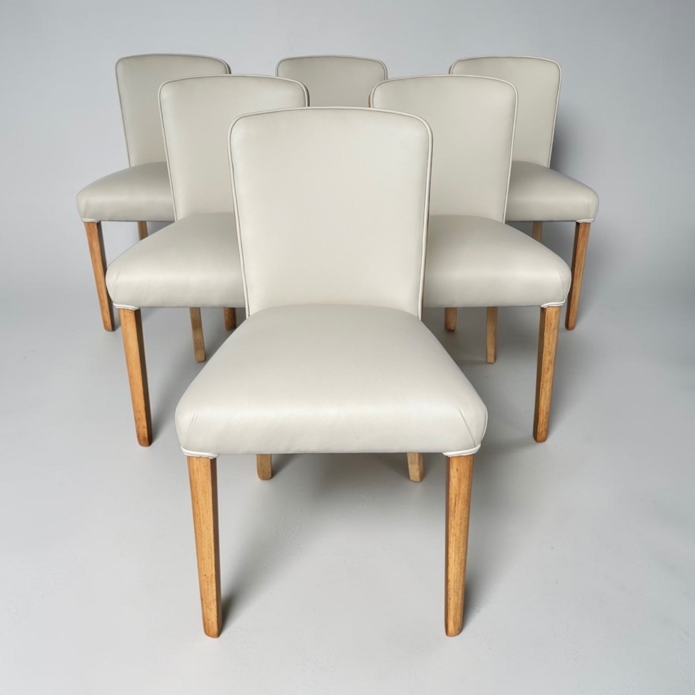 An Art Deco burr walnut dining table featuring rounded corners and a central pedestal base, accompanied by six matching cloud-back chairs upholstered in off-white leather. View IV