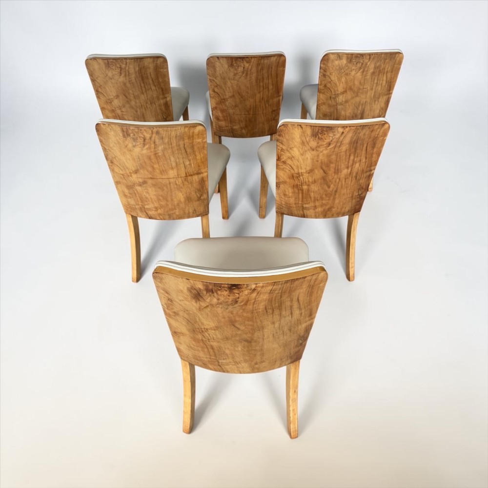 An Art Deco burr walnut dining table featuring rounded corners and a central pedestal base, accompanied by six matching cloud-back chairs upholstered in off-white leather. View V