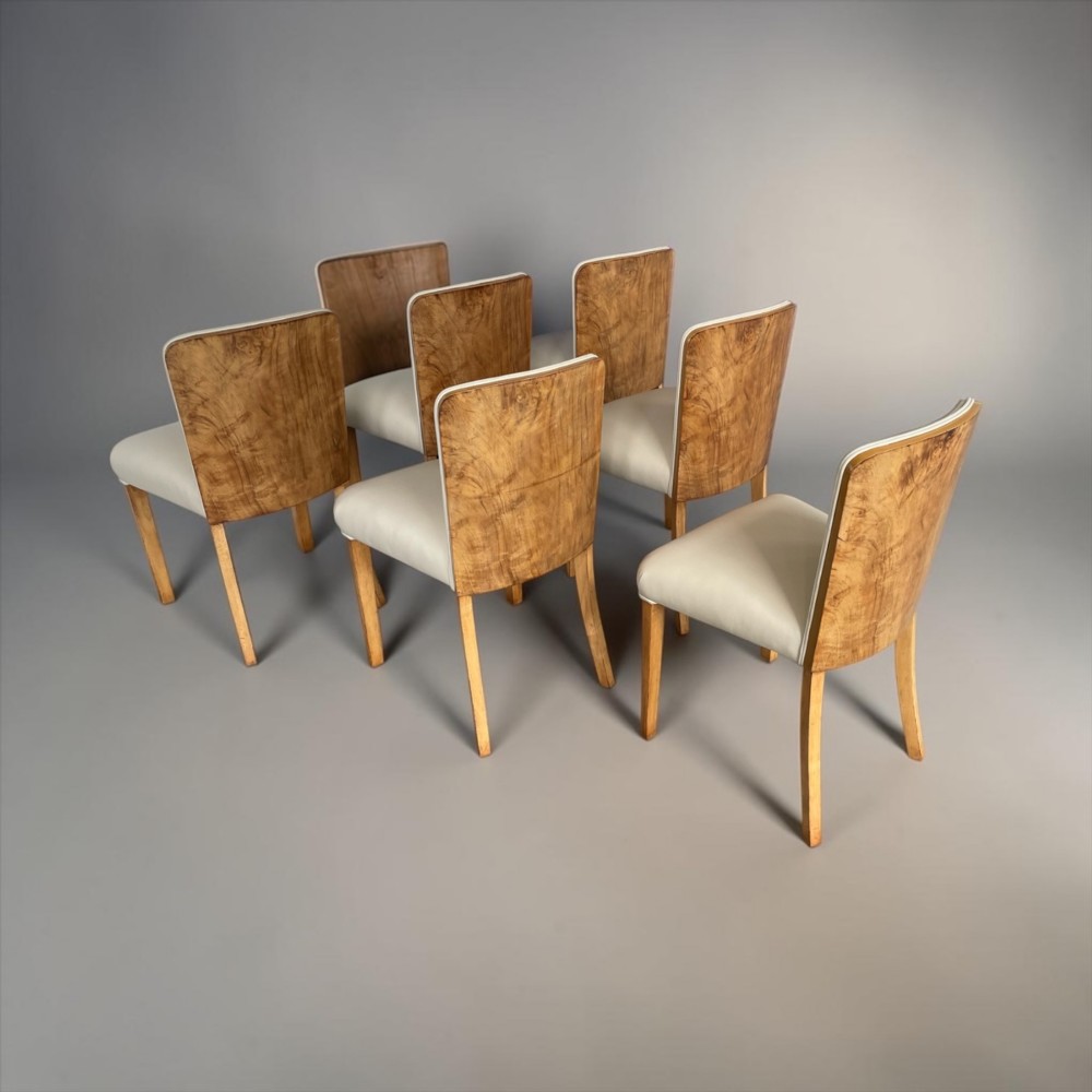 An Art Deco burr walnut dining table featuring rounded corners and a central pedestal base, accompanied by six matching cloud-back chairs upholstered in off-white leather. View VI