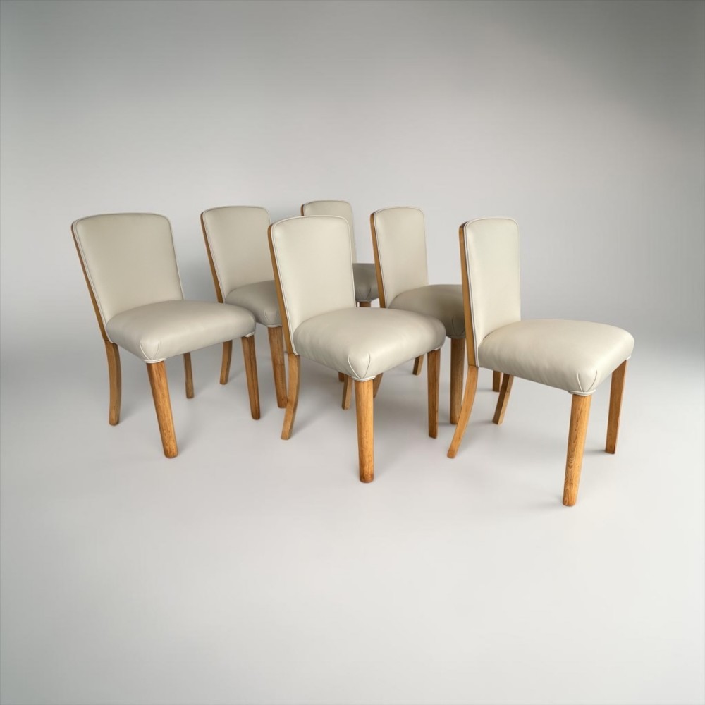 An Art Deco burr walnut dining table featuring rounded corners and a central pedestal base, accompanied by six matching cloud-back chairs upholstered in off-white leather. View VII