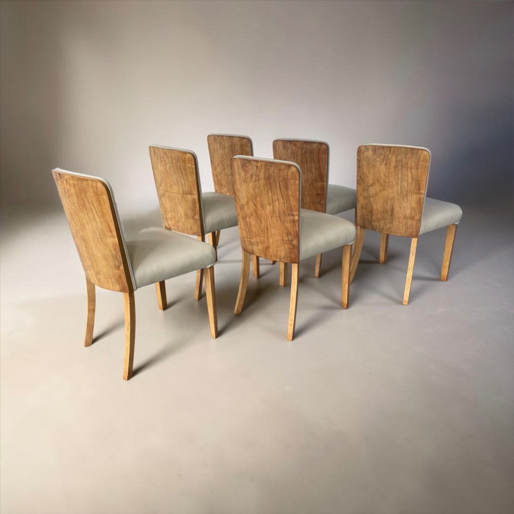 An Art Deco burr walnut dining table featuring rounded corners and a central pedestal base, accompanied by six matching cloud-back chairs upholstered in off-white leather. View VIII