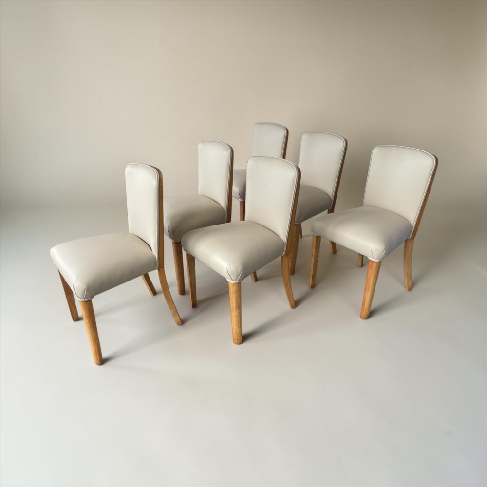An Art Deco burr walnut dining table featuring rounded corners and a central pedestal base, accompanied by six matching cloud-back chairs upholstered in off-white leather. View IX