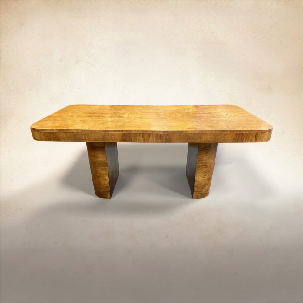 An Art Deco burr walnut dining table featuring rounded corners and a central pedestal base, accompanied by six matching cloud-back chairs upholstered in off-white leather. View X