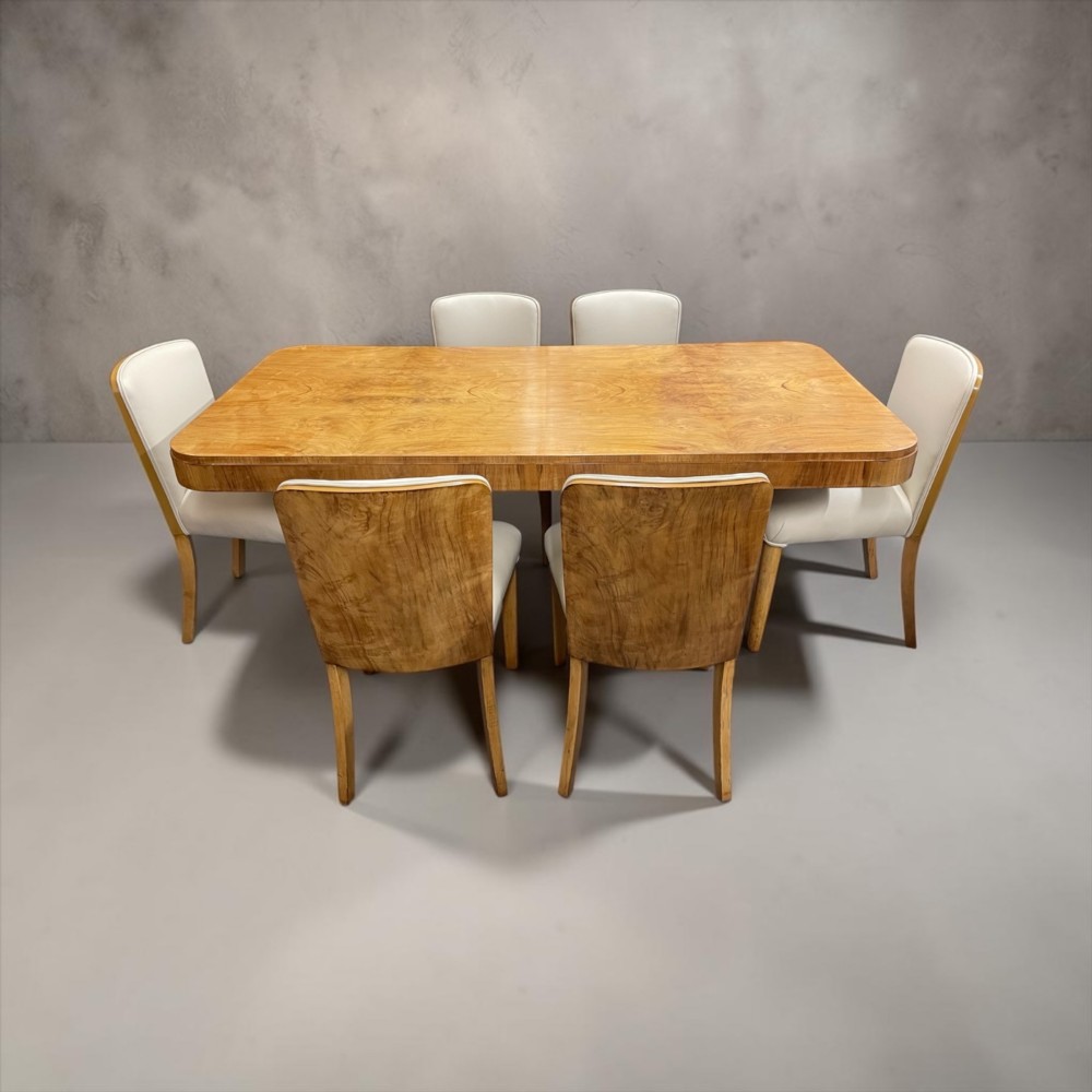 An Art Deco burr walnut dining table featuring rounded corners and a central pedestal base, accompanied by six matching cloud-back chairs upholstered in off-white leather. View XII