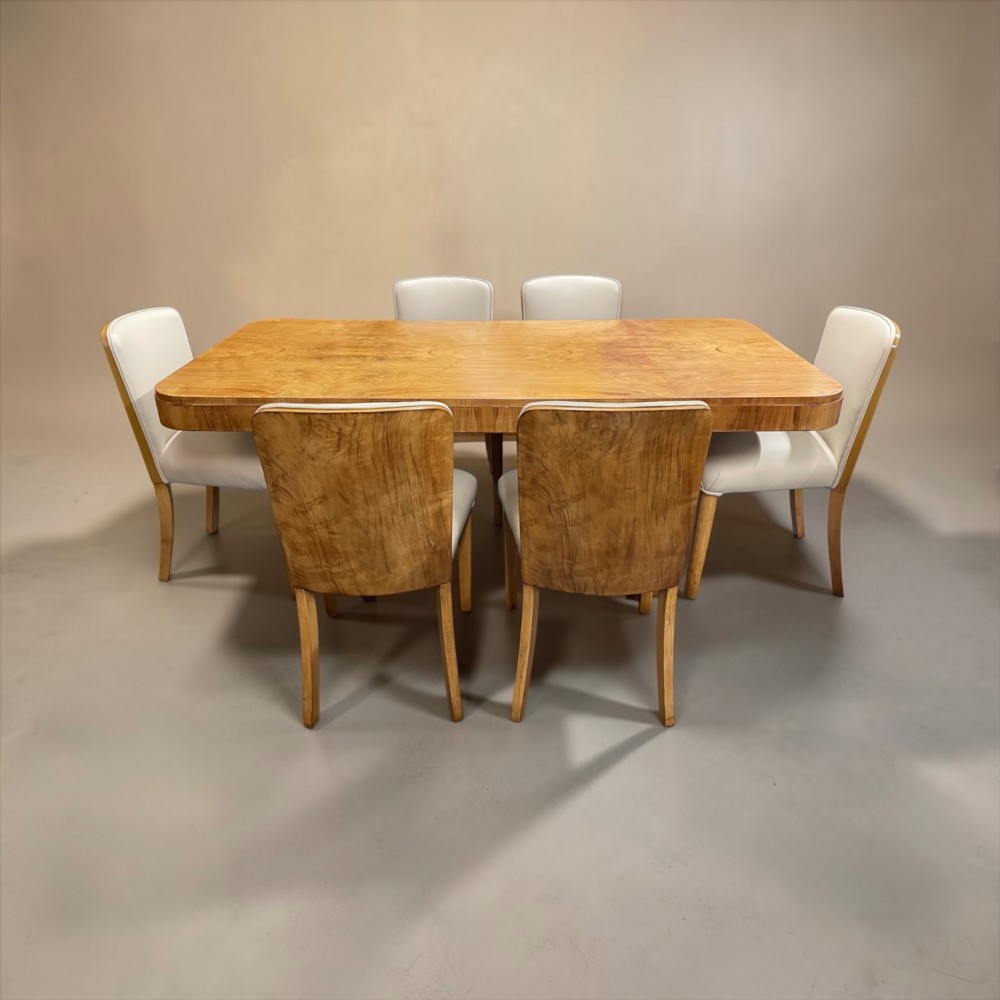 An Art Deco burr walnut dining table featuring rounded corners and a central pedestal base, accompanied by six matching cloud-back chairs upholstered in off-white leather. View XIII
