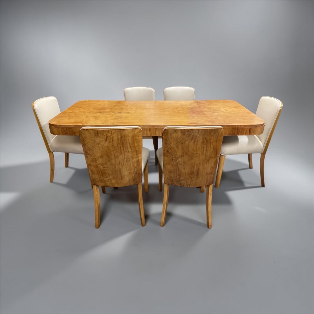 An Art Deco burr walnut dining table featuring rounded corners and a central pedestal base, accompanied by six matching cloud-back chairs upholstered in off-white leather. View XIV