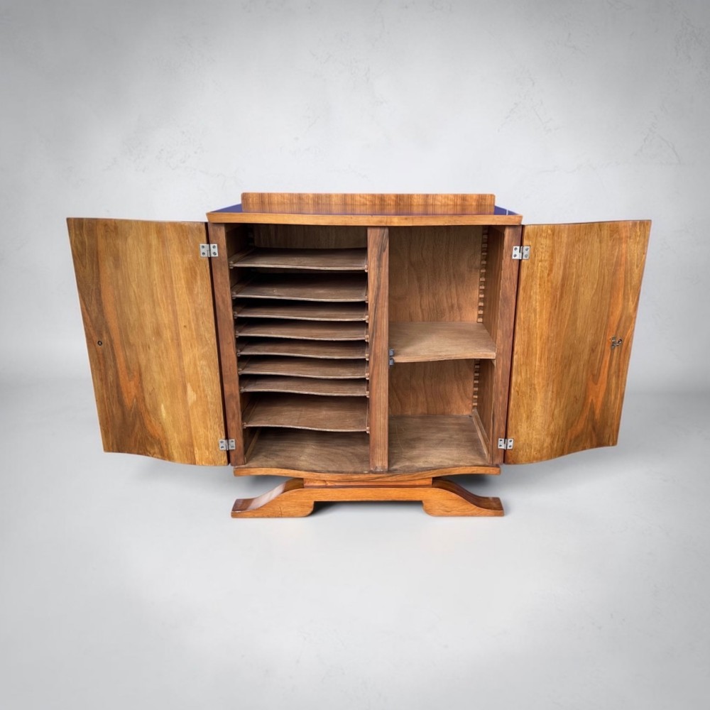 An Art Deco walnut sheet music cabinet with a curved front profile, double doors, metal knobs, and a curved base. View II