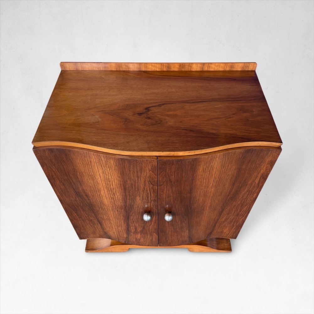 An Art Deco walnut sheet music cabinet with a curved front profile, double doors, metal knobs, and a curved base. View III