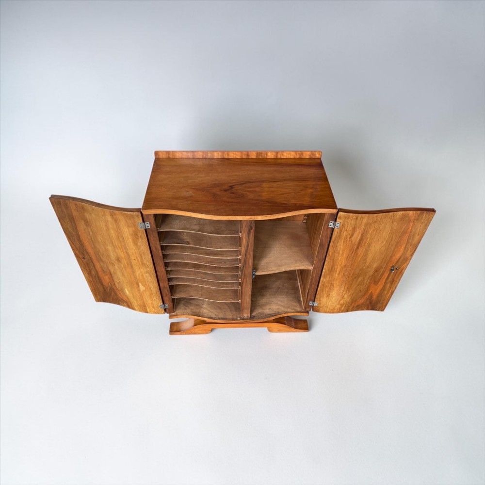 An Art Deco walnut sheet music cabinet with a curved front profile, double doors, metal knobs, and a curved base. View IV