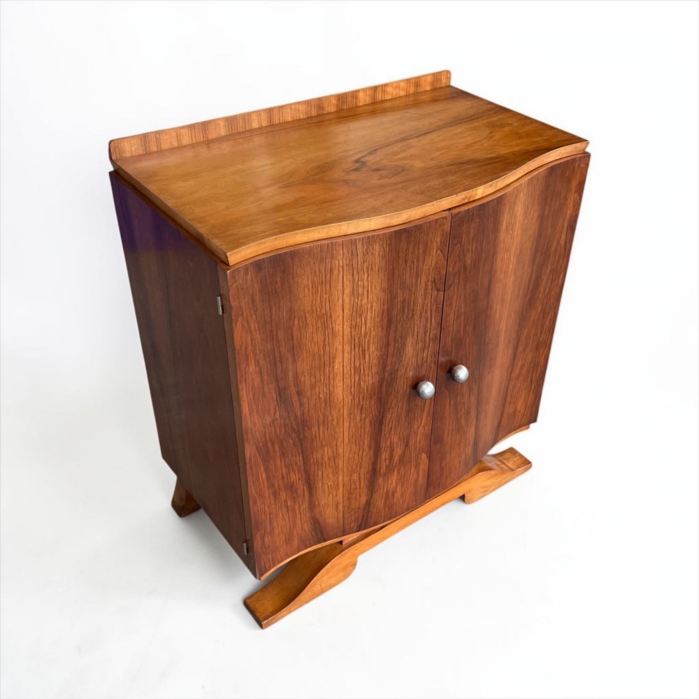 An Art Deco walnut sheet music cabinet with a curved front profile, double doors, metal knobs, and a curved base. View V