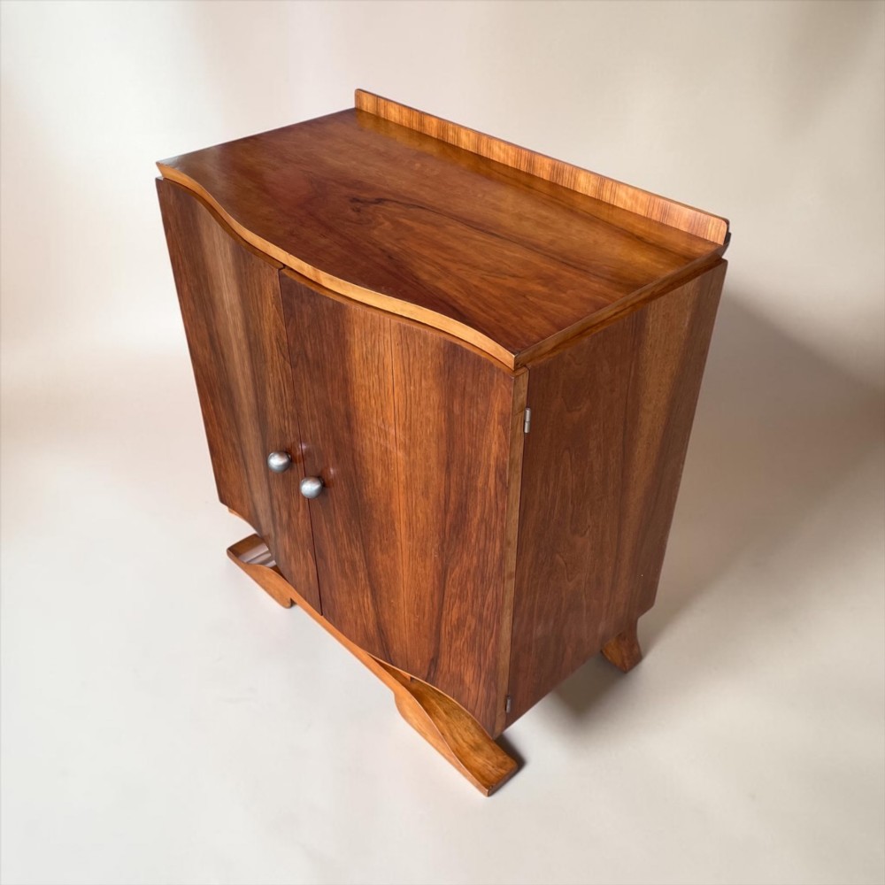 An Art Deco walnut sheet music cabinet with a curved front profile, double doors, metal knobs, and a curved base. View VI