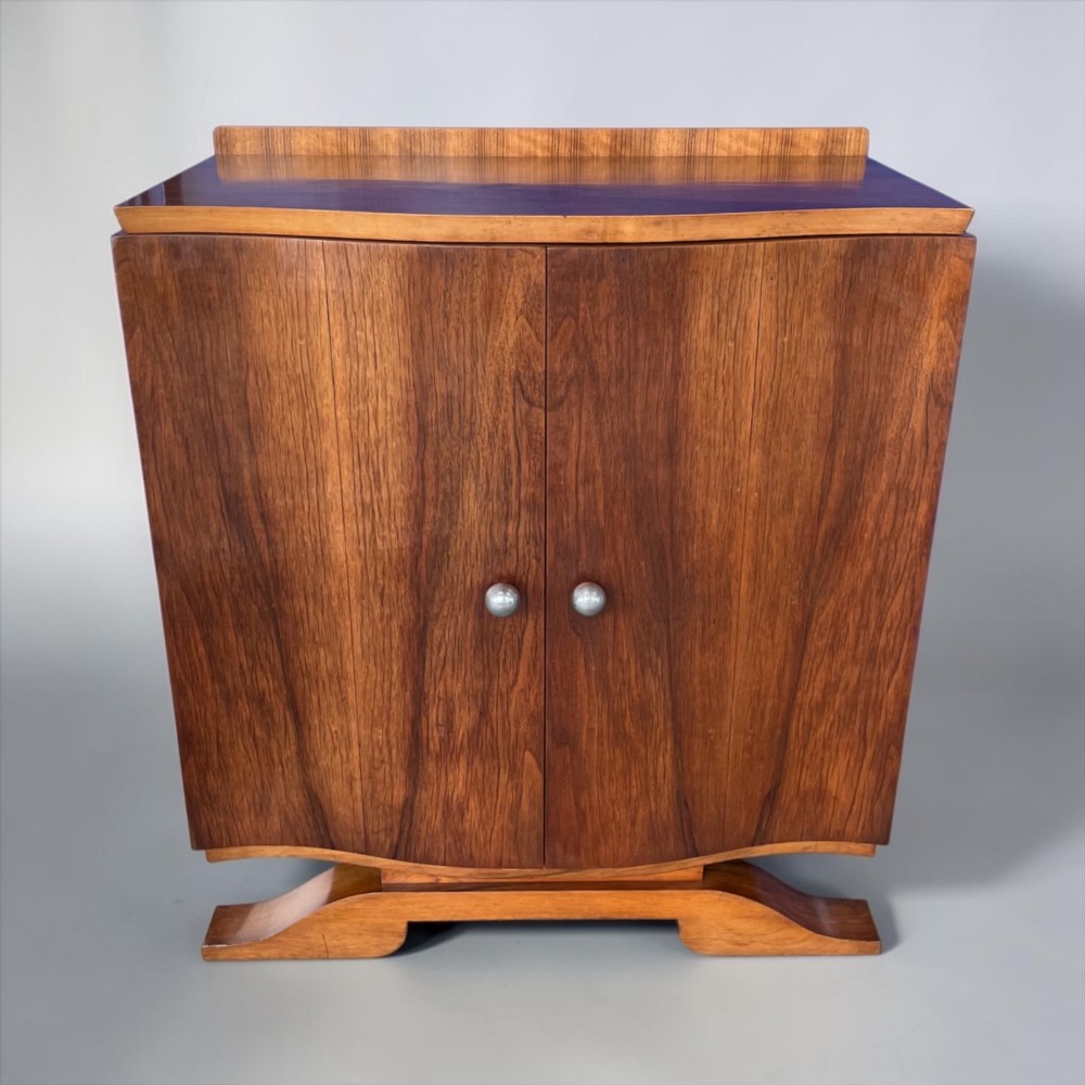 An Art Deco walnut sheet music cabinet with a curved front profile, double doors, metal knobs, and a curved base. View VII