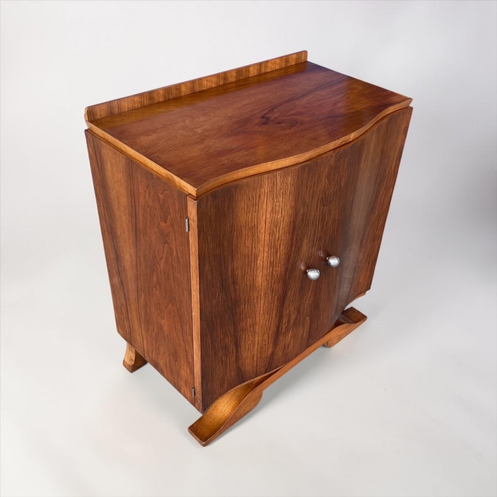 An Art Deco walnut sheet music cabinet with a curved front profile, double doors, metal knobs, and a curved base. View VIII
