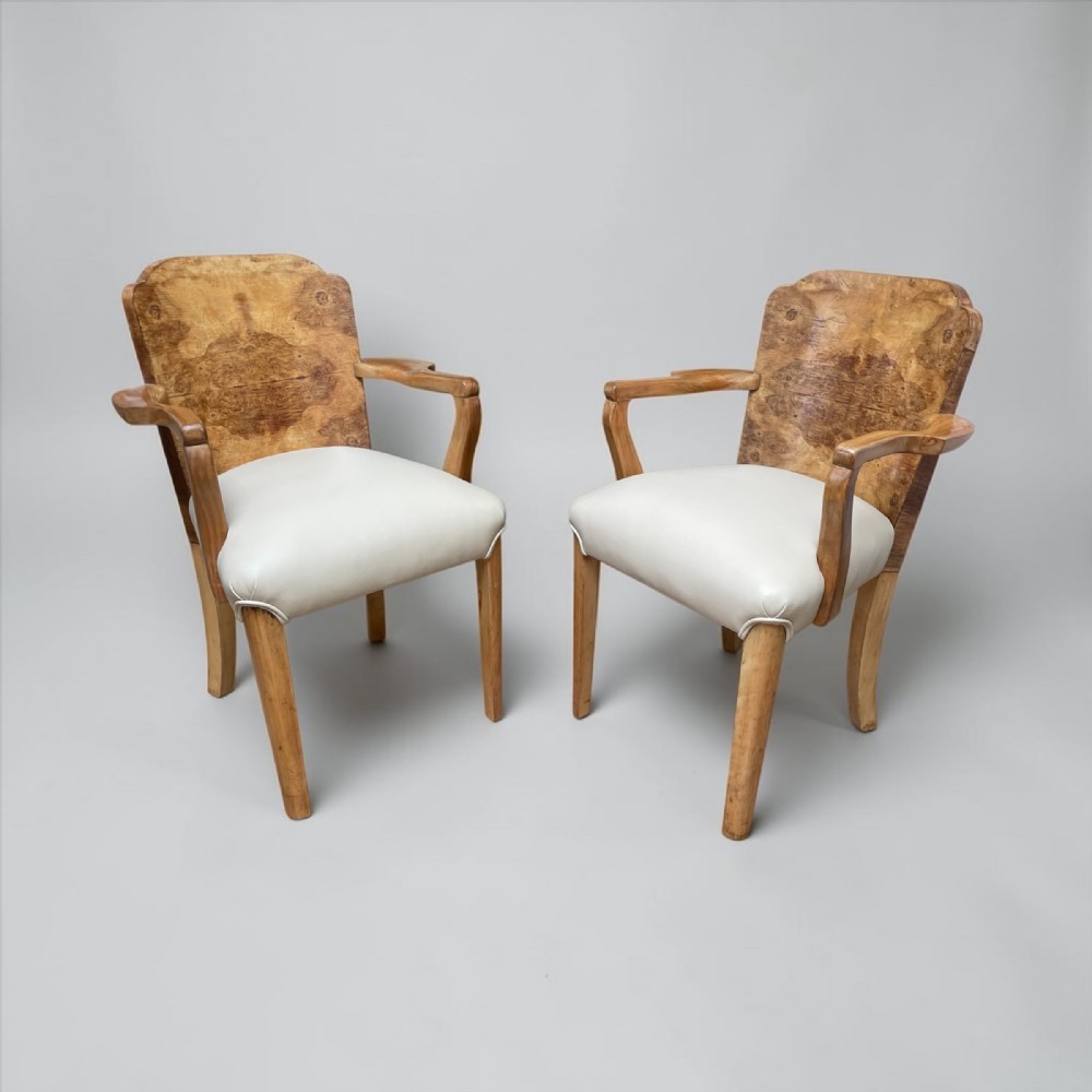 A pair of Art Deco occasional chairs featuring figure-grained burr wood backs, curved wooden armrests, and white leather seats.
