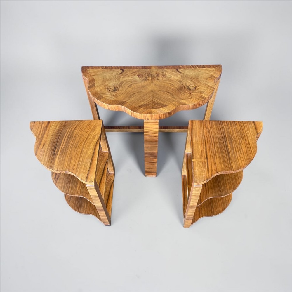 An Art Deco nest of three walnut tables featuring bookmatched wood grain and scalloped tiered edges.