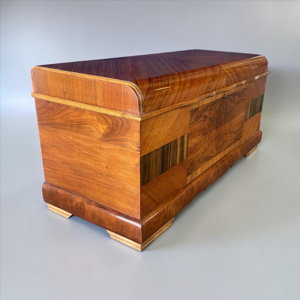 An Art Deco walnut blanket chest featuring geometric bookmatched veneers, curved top edges, and a stepped plinth base.