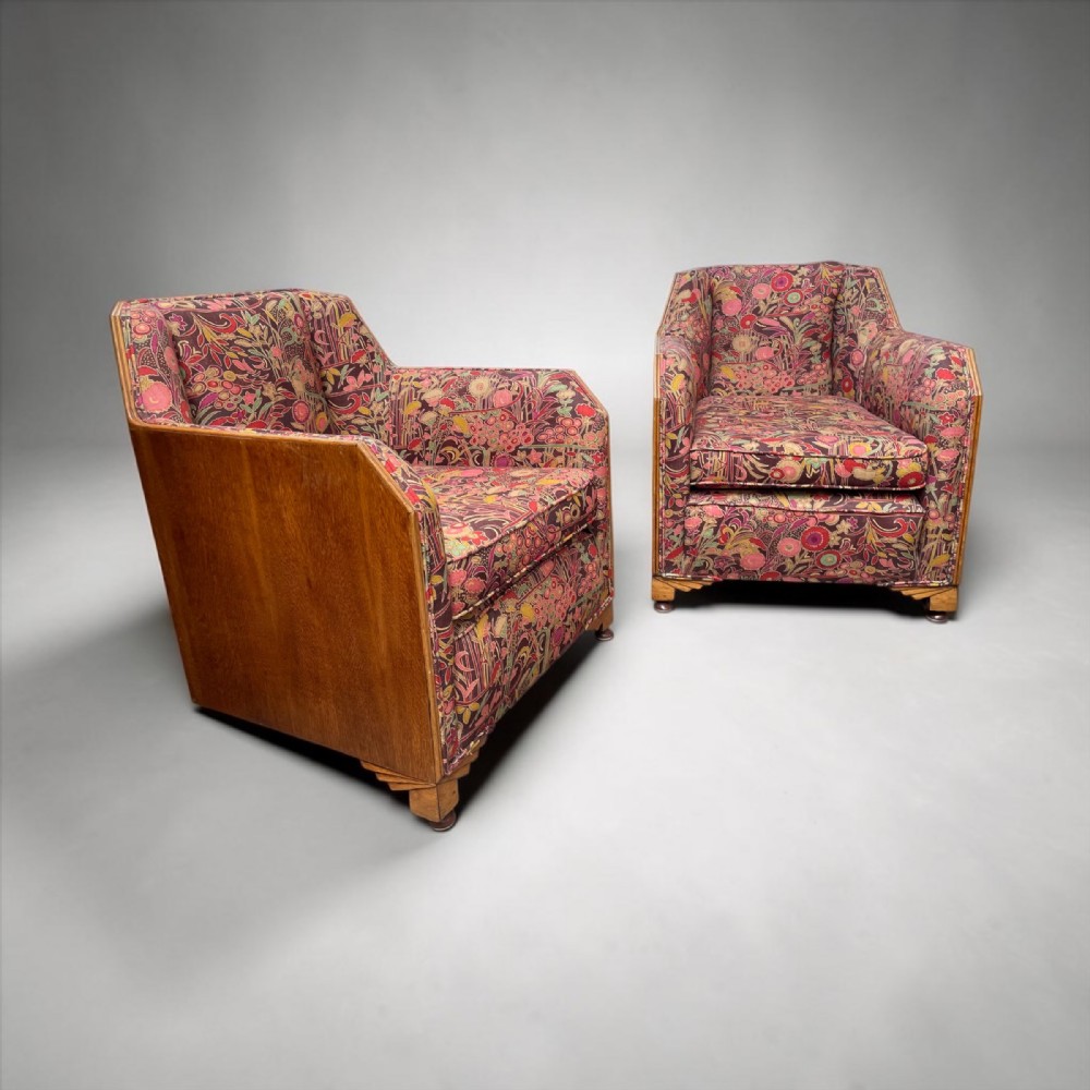 A pair of Art Deco armchairs featuring geometric wooden side frames and multi-coloured patterned floral upholstery.