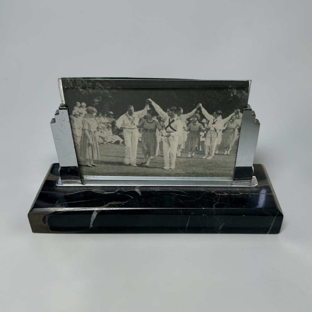 An Art Deco photo frame featuring a heavy black marble base with white veining and stepped chrome side brackets holding a glass display pane.