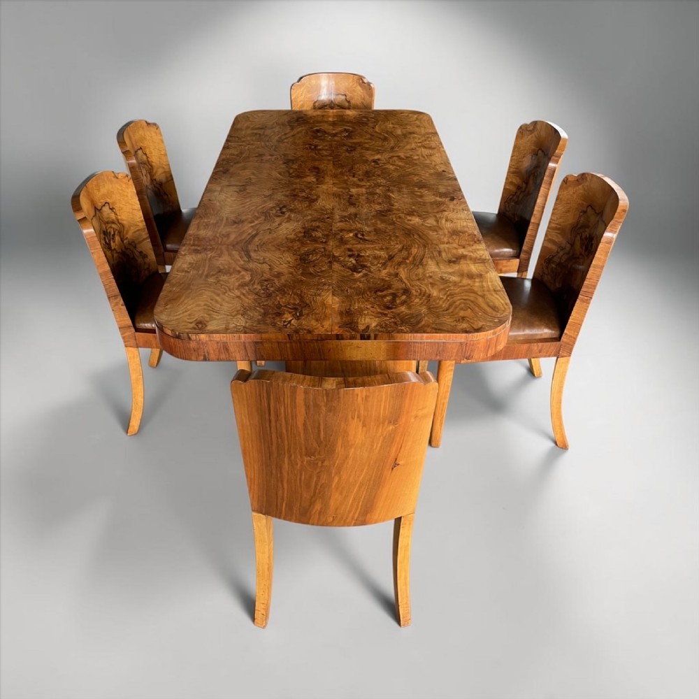 An Art Deco burr walnut dining table accompanied by six matching chairs with curved backrests and dark brown leather seats.