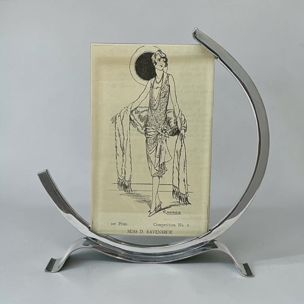 An Art Deco chrome picture frame featuring a curved crescent-shaped metal stand holding a vertical rectangular glass pane.