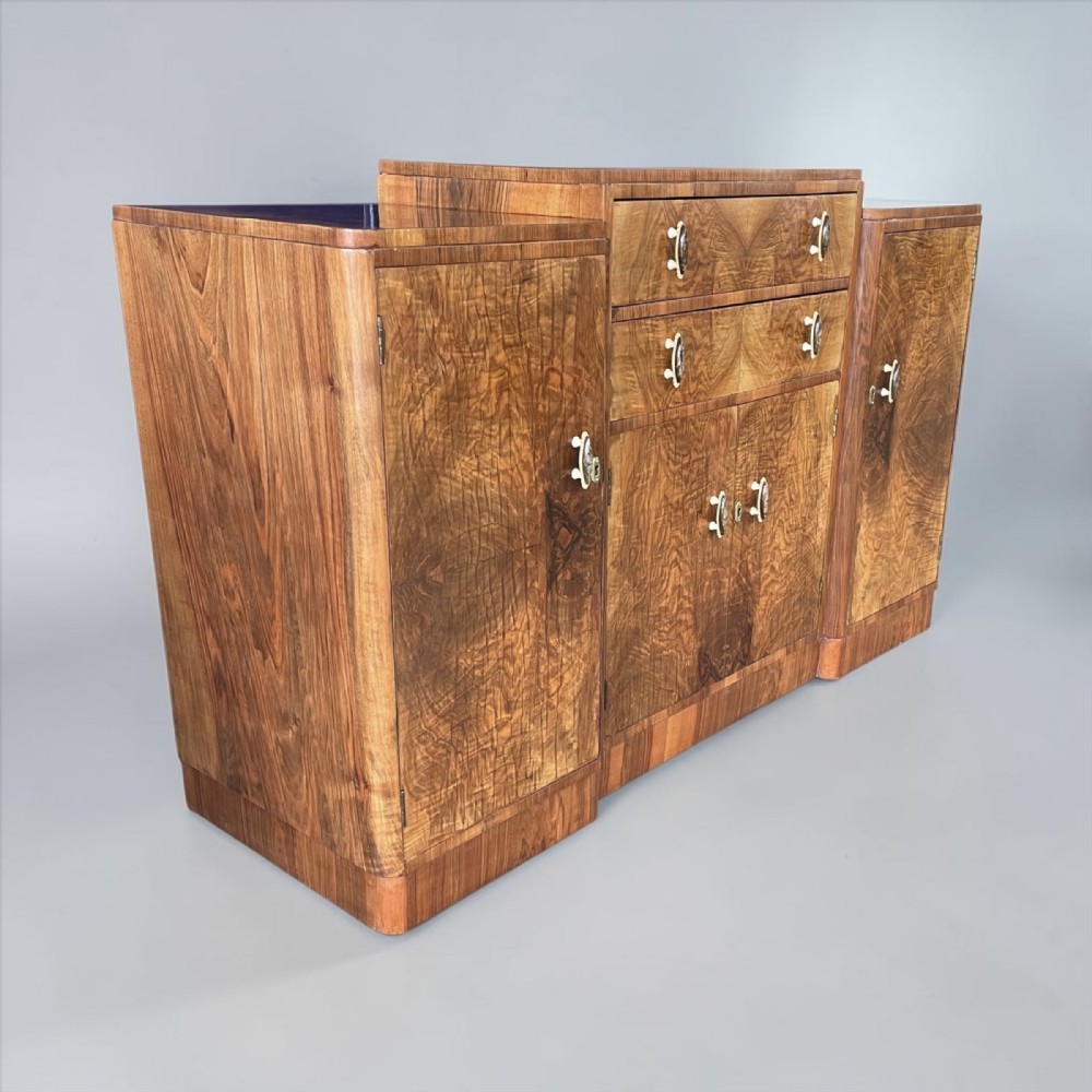 An Art Deco sideboard made of figured walnut veneer with rounded corners, double central drawers, twin side cupboards, and decorative drop handles.