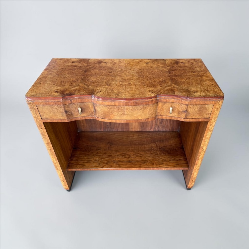 An Art Deco burr walnut serving table featuring a shaped serpentine front, drawers with metal pulls, and an open lower shelf.