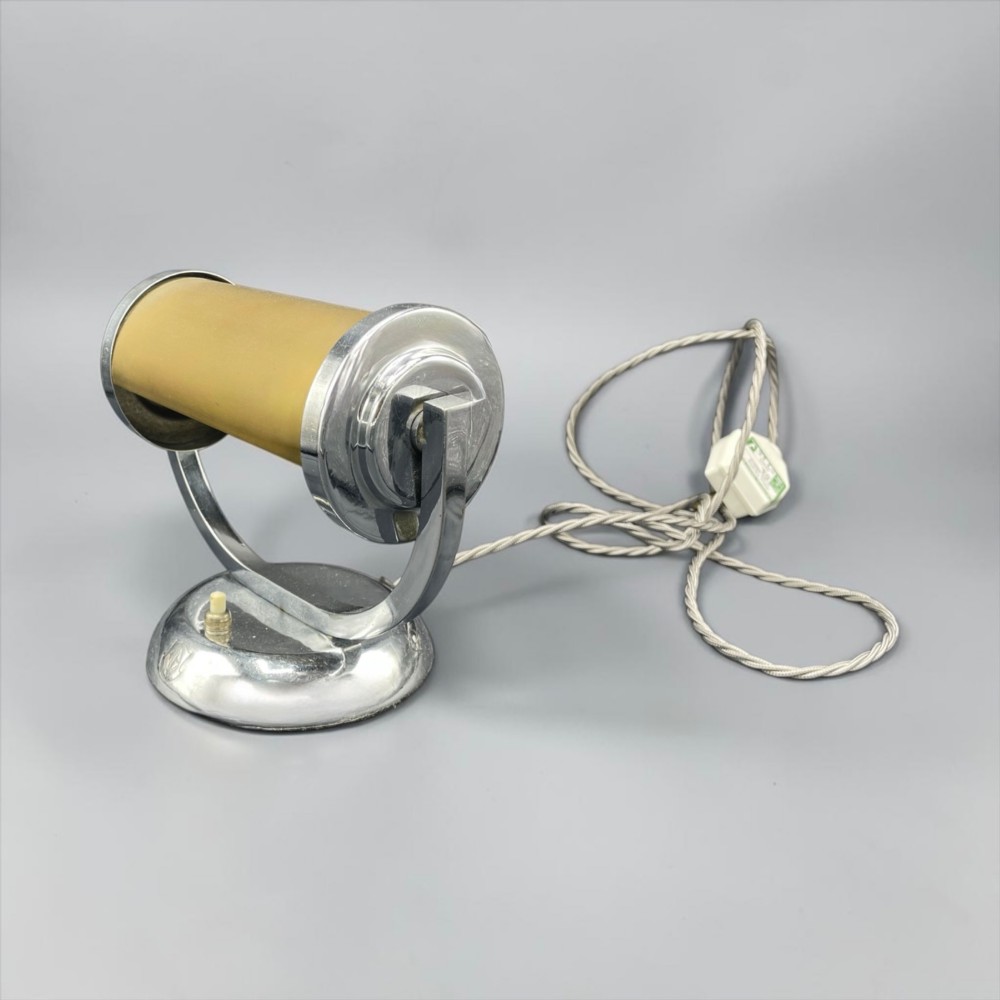 An Art Deco chrome desk lamp featuring a cylindrical beige glass shade supported by a curved metal arm on a round chrome base.