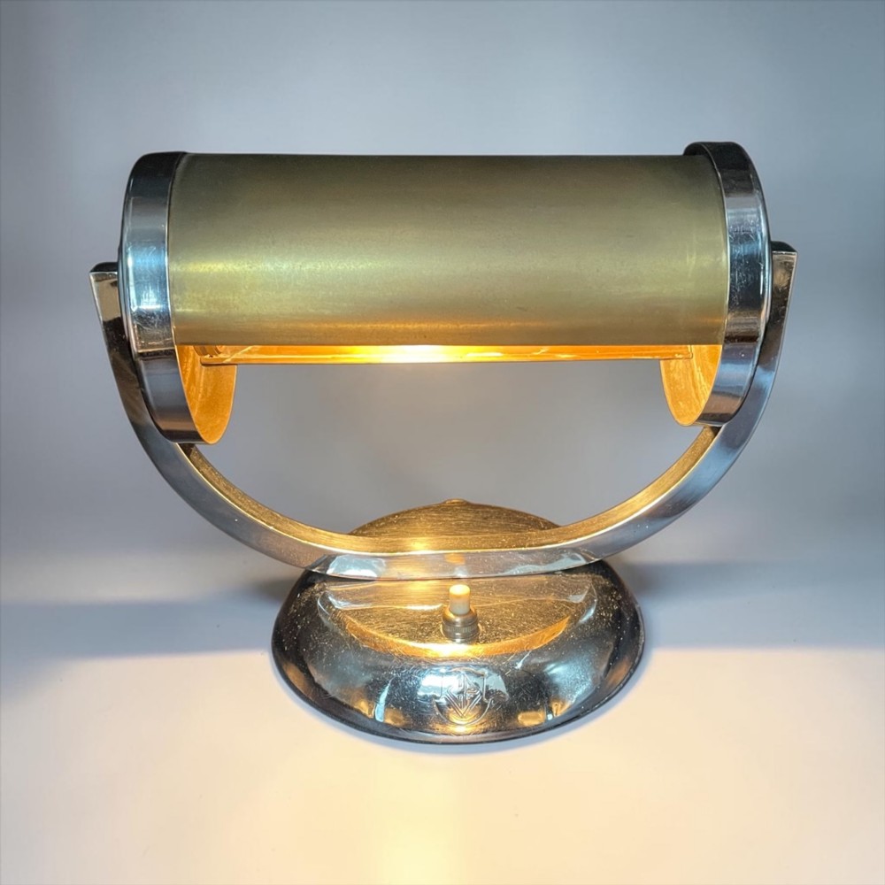 An Art Deco chrome desk lamp featuring a cylindrical beige glass shade supported by a curved metal arm on a round chrome base. View II