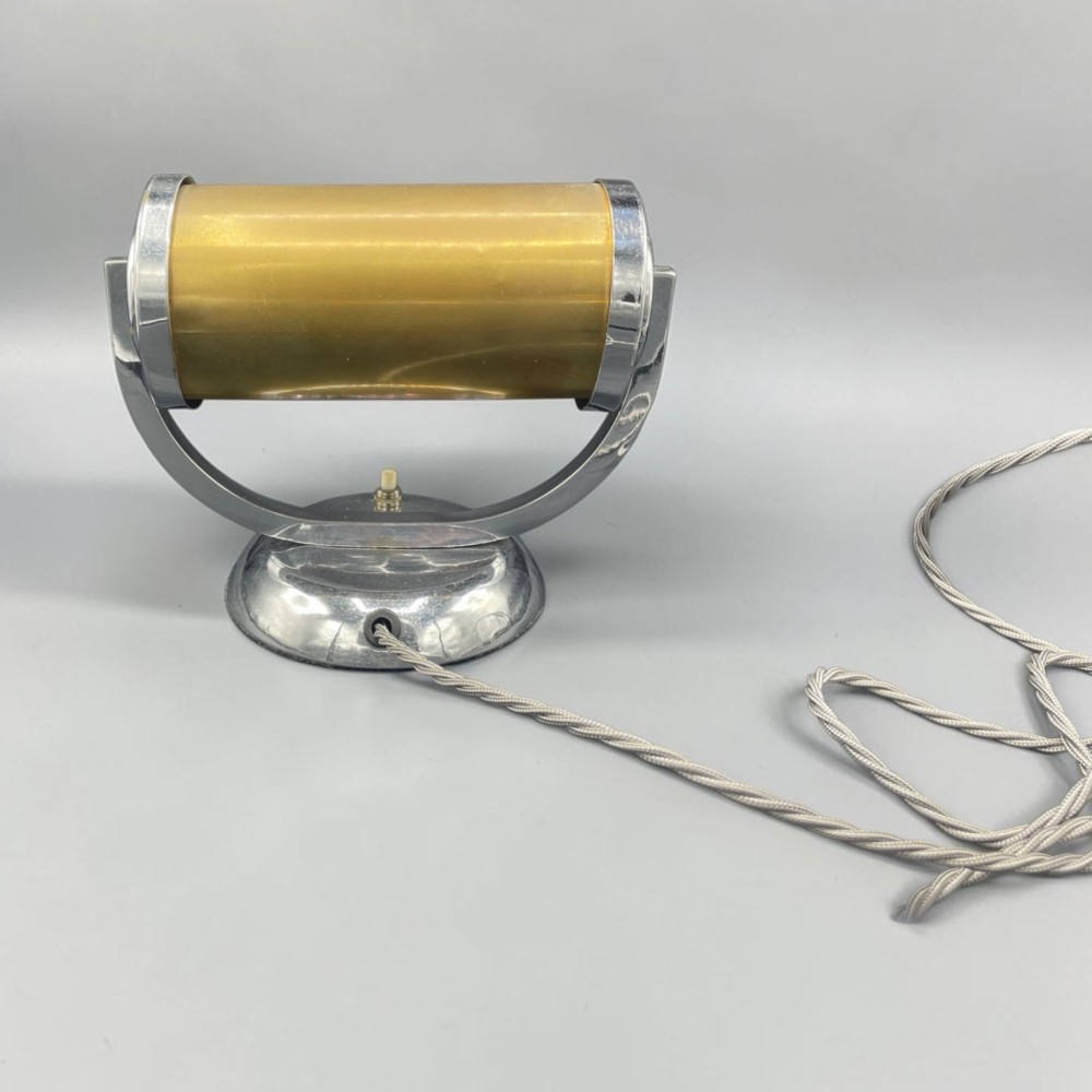 An Art Deco chrome desk lamp featuring a cylindrical beige glass shade supported by a curved metal arm on a round chrome base. View IV