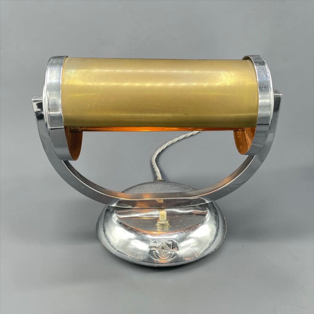 An Art Deco chrome desk lamp featuring a cylindrical beige glass shade supported by a curved metal arm on a round chrome base. View VI