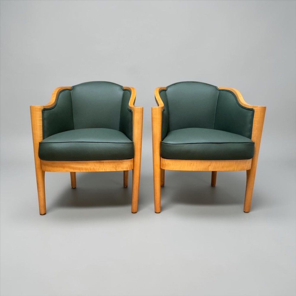 A pair of British Art Deco occasional chairs with curved light honey-toned timber frames and dark green leather upholstered seats and backrests.