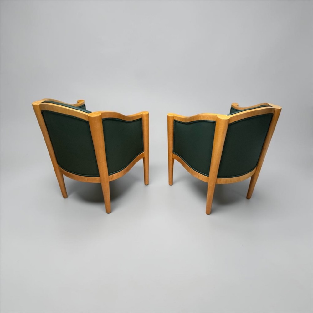 A pair of British Art Deco occasional chairs with curved light honey-toned timber frames and dark green leather upholstered seats and backrests. View X